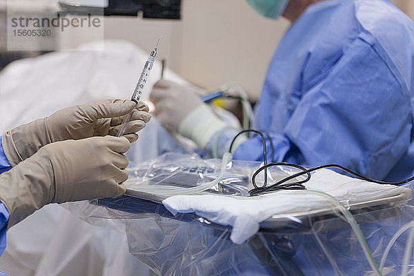 Chirurgische Technologin reicht dem Arzt eine sterile Spritze mit intraokularer Spüllösung