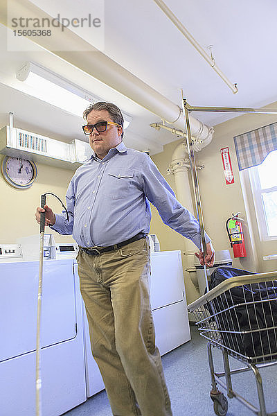 Mann mit angeborener Blindheit legt seine Wäsche in den Wäschewagen in der Waschküche