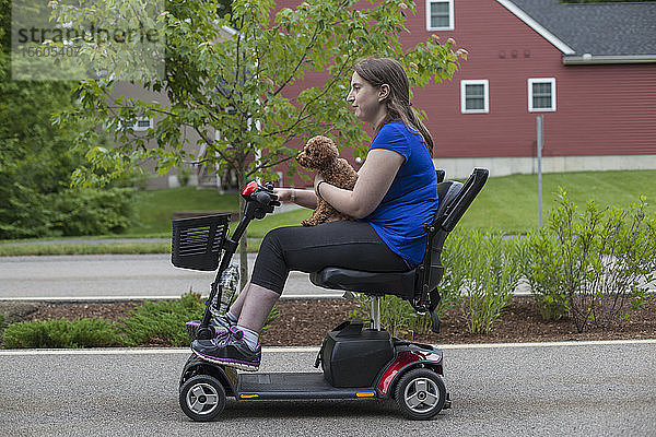 Junge Frau mit zerebraler Lähmung fährt mit ihrem Hund auf dem Roller