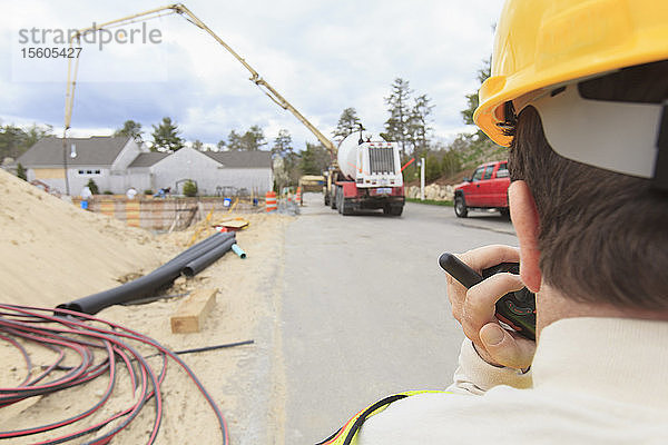 Bauleiter mit Querschnittslähmung am Walkie-Talkie zur Betonpumpe beim Gießen des Fundaments