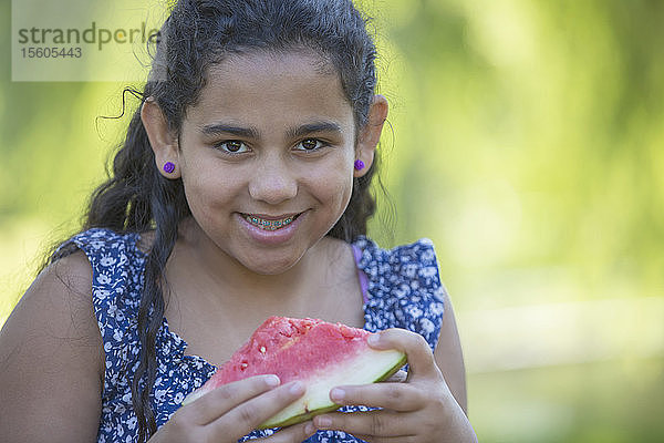 Porträt eines glücklichen hispanischen Teenagers  der eine Wassermelone mit Zahnspange isst