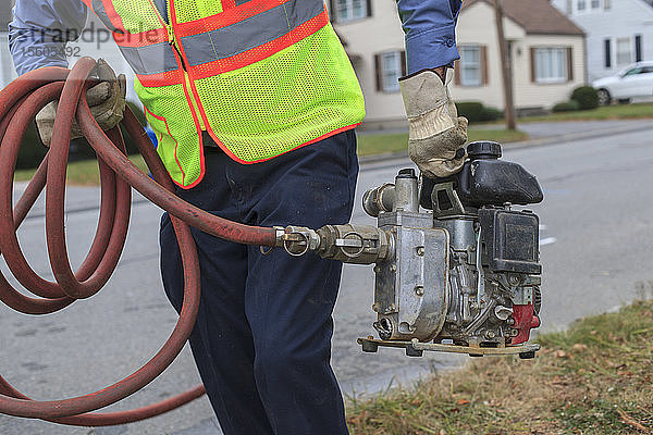 Techniker der Wasserbehörde trägt eine benzinbetriebene Pumpe zum Spülen von Hydranten