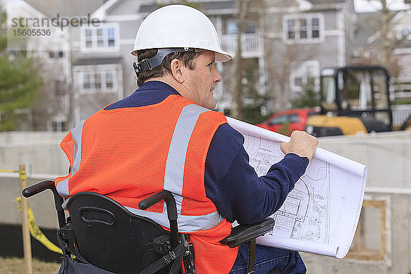 Bauingenieur mit Rückenmarksverletzung mit Hausplänen auf der Baustelle