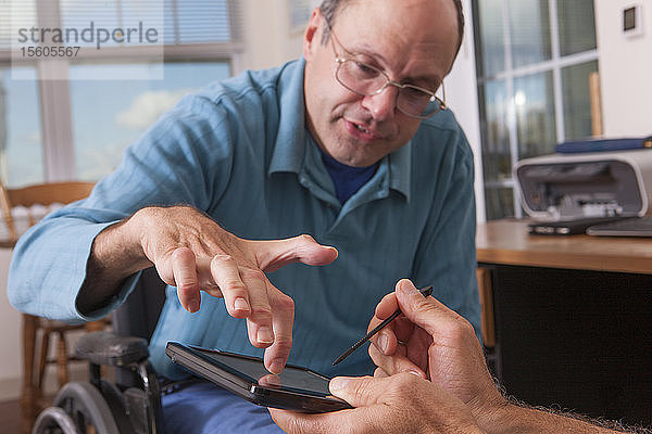 Zwei behinderte Männer  die in Rollstühlen sitzen und ein digitales Tablet benutzen  einer mit deformierten Händen