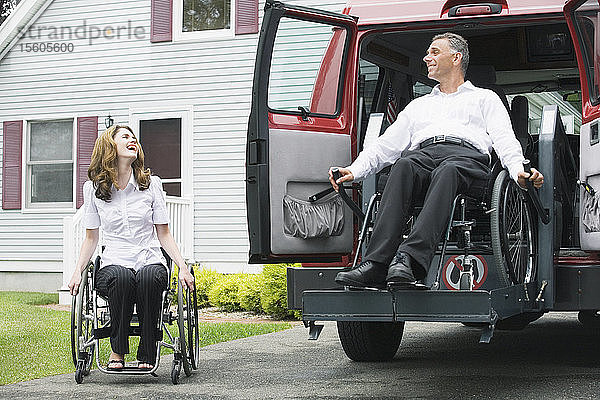Eine Frau im mittleren Erwachsenenalter sitzt in einem Rollstuhl und schaut auf einen Mann im mittleren Erwachsenenalter  der mit einer Rückenmarksverletzung aus einem Rollstuhllift heruntergelassen wird