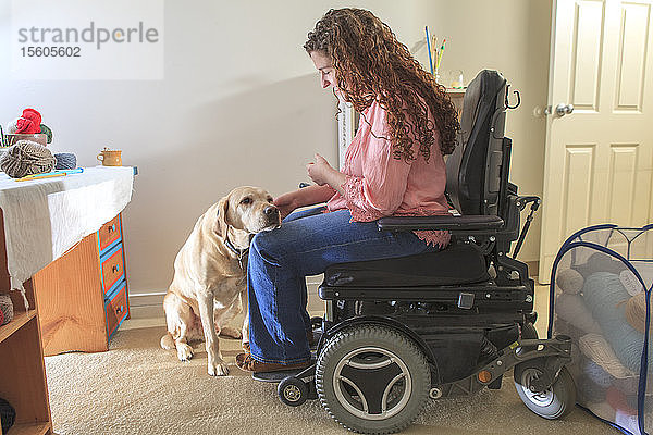 Frau mit Muskeldystrophie streichelt ihren Diensthund in ihrem Büro