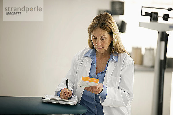 Mittlerer erwachsener Arzt  der sich Notizen macht  während er eine Schachtel mit medizinischem Material liest