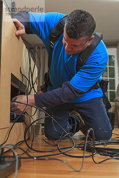 Kabelinstallateur bei der Arbeit in einer Wohnung hinter dem Fernseher