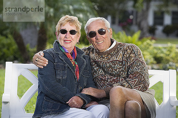 Porträt eines lächelnden älteren Paares  das auf einer Bank in einem Park sitzt.