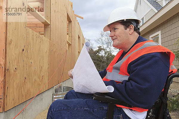 Bauingenieur mit Querschnittslähmung hält Hauspläne auf der Baustelle