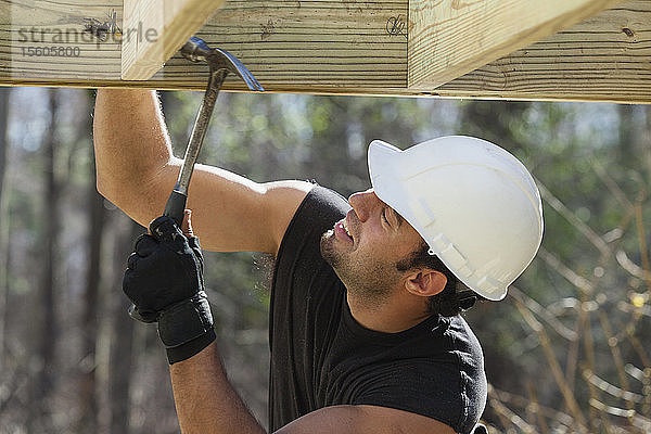 Hispanischer Zimmermann nagelt druckbehandelten Terrassenbalken mit Hammer