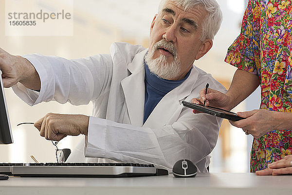 Arzt und Krankenschwester in einer Konferenz mit Computer und Tablet. Arzt hat Muskeldystrophie