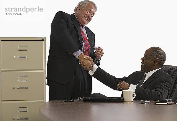 Zwei Geschäftsleute schütteln sich die Hände und lächeln in einem Büro