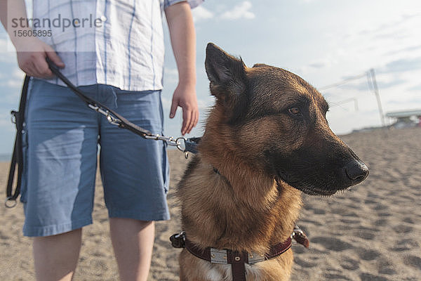 Blinder Mann geht mit seinem Diensthund am Strand entlang