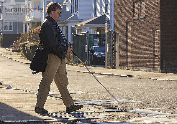 Ein Mann mit angeborener Blindheit überquert die Straße mit seinem Blindenstock