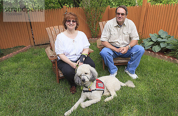 Frau mit RSD und ihr Diensthund mit Ehemann sitzen in ihrem Hinterhof