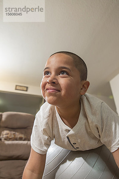 Glücklicher hispanischer Junge mit Autismus  der mit einem Übungsball im Wohnzimmer spielt