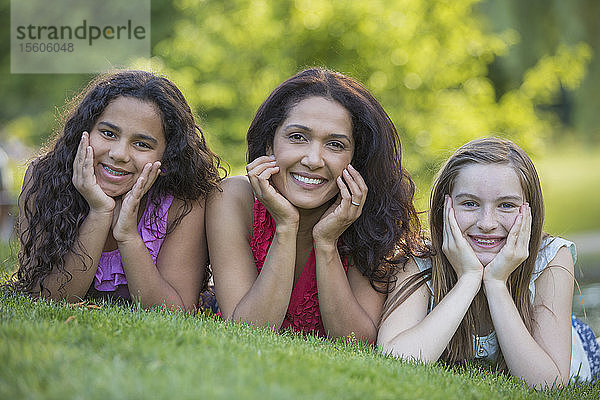 Porträt einer glücklichen hispanischen Mutter mit zwei Teenager-Töchtern  die Zahnspangen tragen und in einem Park lächeln
