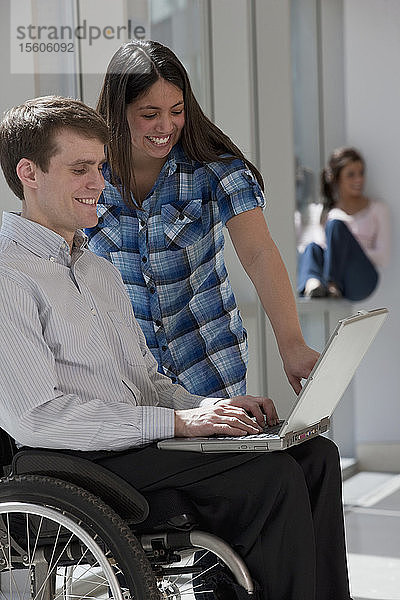 Rückenmarkverletzter Lehrer  der einen Laptop benutzt  während ein Schüler neben ihm steht