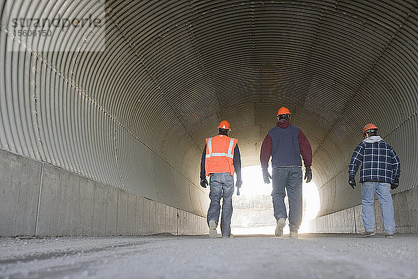 Drei Ingenieure gehen in einem Tunnel in einem Asphaltwerk