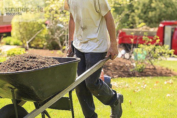 Landschaftsgärtner trägt Mulch in einer Schubkarre in einen Garten