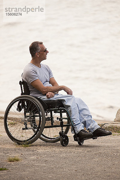 Mann mit Querschnittslähmung sitzt im Rollstuhl am Meer