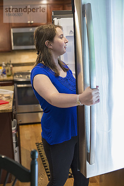 Junge Frau mit zerebraler Lähmung öffnet Kühlschrank zu Hause