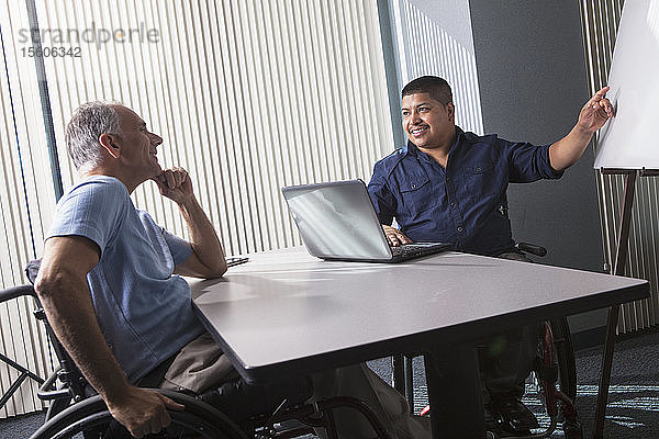 Zwei Männer mit Rückenmarksverletzungen bei der Arbeit mit einer Präsentationstafel in einem Büro