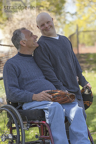Glücklicher Vater mit Rückenmarksverletzung und sein Sohn mit Down-Syndrom beim Baseballspielen im Park