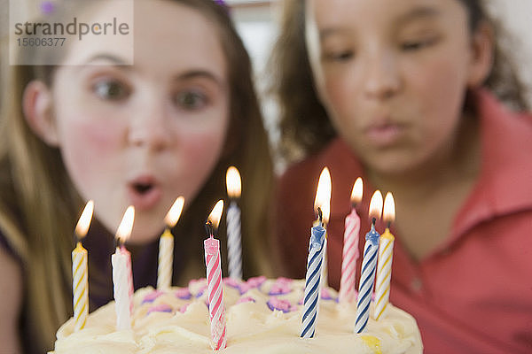 Zwei Mädchen blasen die Kerzen auf einer Geburtstagstorte aus