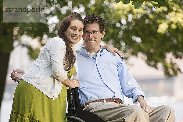Schwangere Frau umarmt ihren Mann  der im Rollstuhl sitzt und eine Rückenmarksverletzung hat
