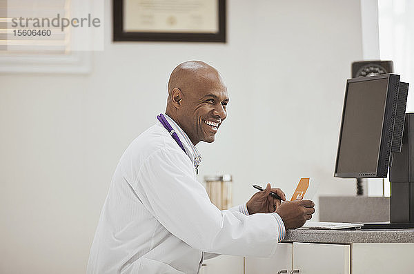 Lachender männlicher Arzt  der eine Schachtel mit Medikamenten in seinem Büro hält