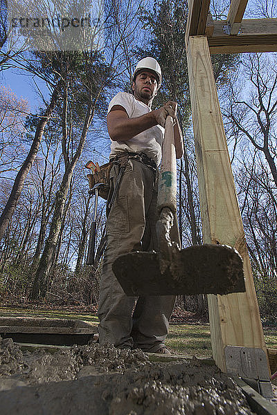 Hispanischer Zimmermann beim Nivellieren von Beton im Treppenfundament