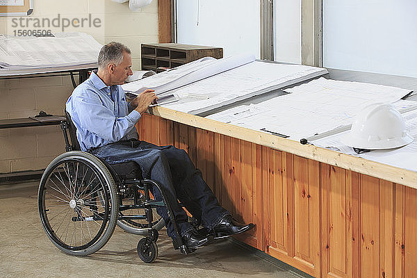 Projektingenieur mit einer Rückenmarksverletzung im Rollstuhl bei der Arbeit an seinem Tablet