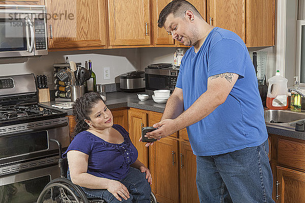 Frau mit Spina Bifida und ihr Mann sehen sich in der Küche eine SMS an