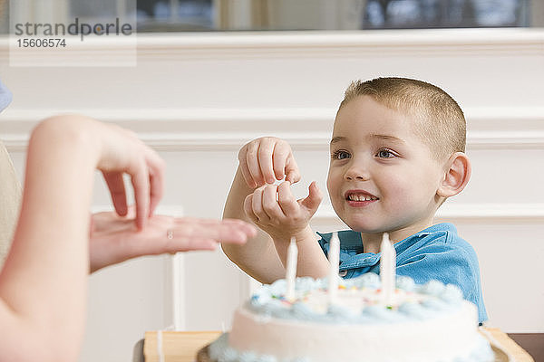 Junge gebärdet das Wort Cake in amerikanischer Zeichensprache vor einer Geburtstagstorte sitzend