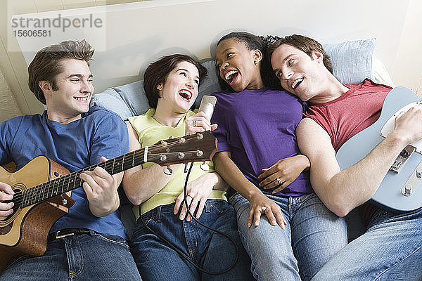 Zwei Männer und eine Frau liegen mit Gitarren und Mikrofon auf einem Bett.