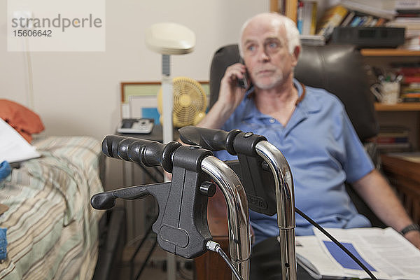 Mann mit Ataxie  der mit seiner Gehhilfe in seinem Schlafzimmer telefoniert