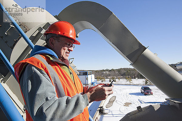 Ingenieur  der in einem Werkstoffwerk im Winter eine SMS auf einem Mobiltelefon schreibt