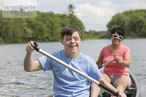 Junger Mann mit Down-Syndrom rudert mit seinem Freund in einem Kanu auf einem See