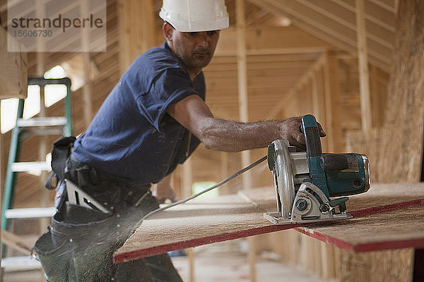 Spanischer Zimmermann beim Beschneiden von Dachplatten mit einer Kreissäge an einem im Bau befindlichen Haus