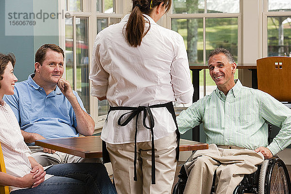Zwei Männer im Rollstuhl mit Rückenmarksverletzungen und ein Freund bestellen Essen in einem Café.