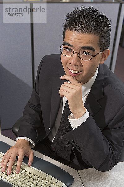 Glücklicher asiatischer Mann mit Autismus arbeitet am Computer in einem Büro