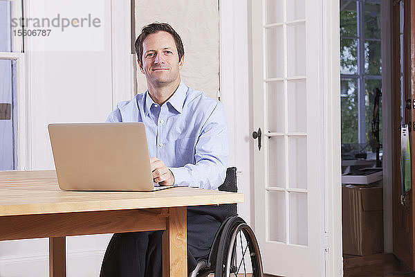 Mann mit Rückenmarksverletzung sitzt im Rollstuhl und arbeitet am Laptop