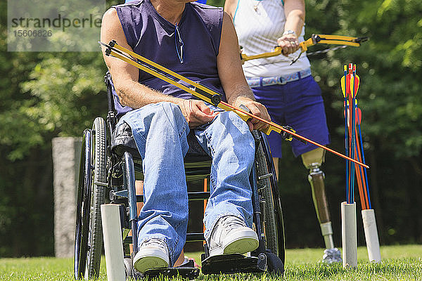 Mann mit Rückenmarksverletzung und Frau mit Beinprothese bereiten Pfeil und Bogen zum Üben vor