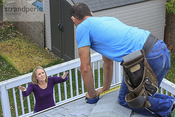 Hausbesitzer  der einem hörgeschädigten Dachdecker auf dem Dach Schindeln in amerikanischer Gebärdensprache gebärdet