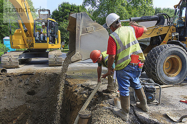 Bauarbeiter füllen ein Loch mit Kies vom Frontlader
