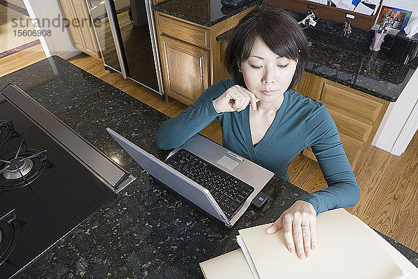 Hochformatige Ansicht einer erwachsenen Frau  die vor einem Laptop sitzt und sich Dokumente ansieht