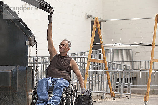 Laderampenarbeiter mit Rückenmarksverletzung im Rollstuhl  der eine Tasche in den Müllcontainer wirft
