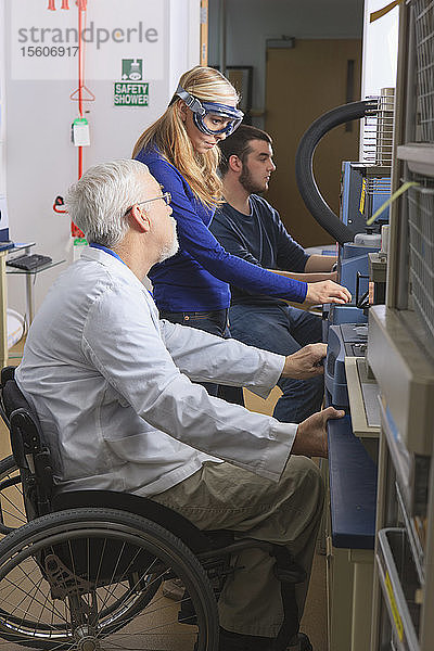 Professor mit Muskeldystrophie berät Ingenieurstudenten im Chemielabor bei der Arbeit an thermogravimetrischen Analysatoren